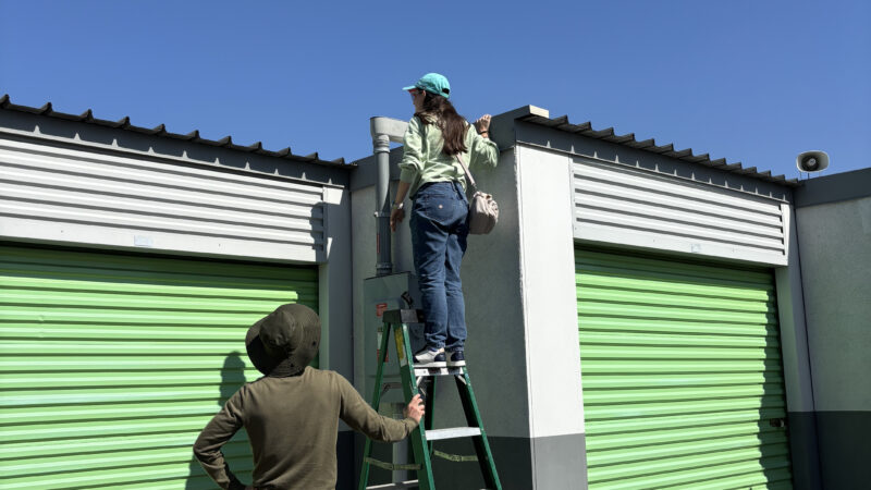 Student standing on ladder to see solar panels on storage facility.