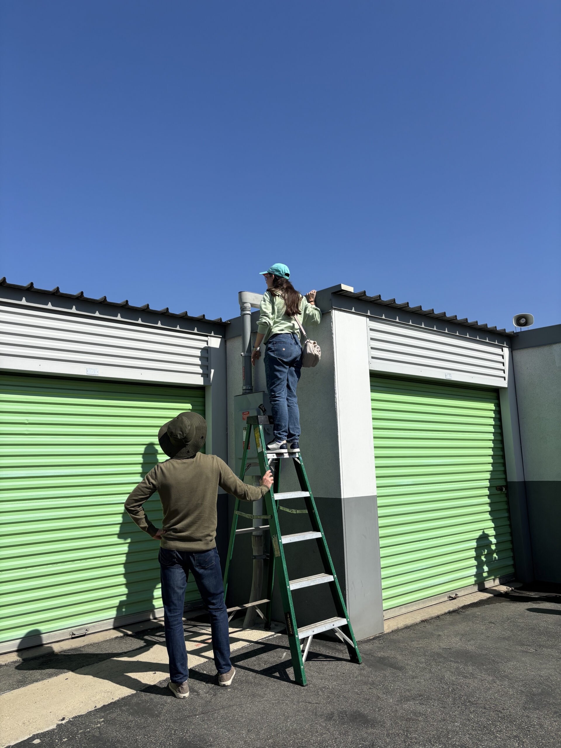 Student standing on ladder to see solar panels on storage facility.